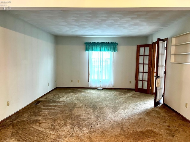 unfurnished room featuring a textured ceiling, dark colored carpet, and french doors