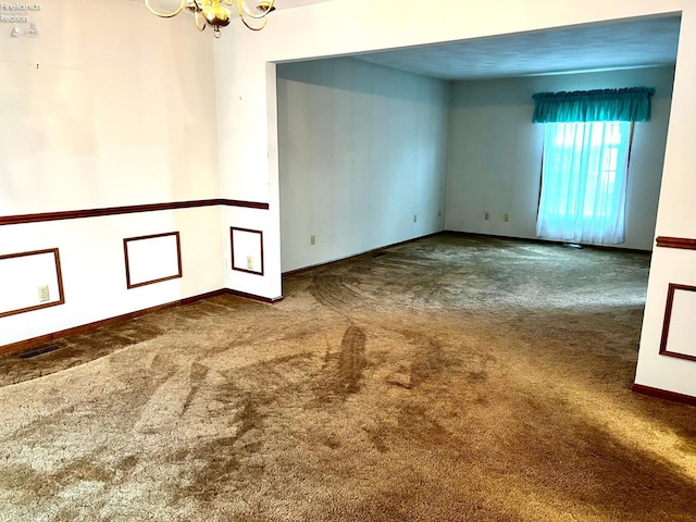 spare room featuring dark carpet and a chandelier