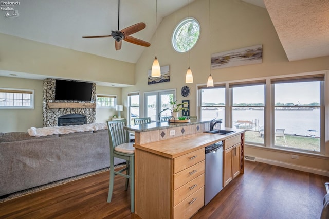 kitchen with ceiling fan, an island with sink, dishwasher, a fireplace, and wood counters