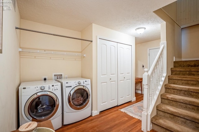 laundry area featuring light wood-type flooring, a textured ceiling, and washing machine and clothes dryer