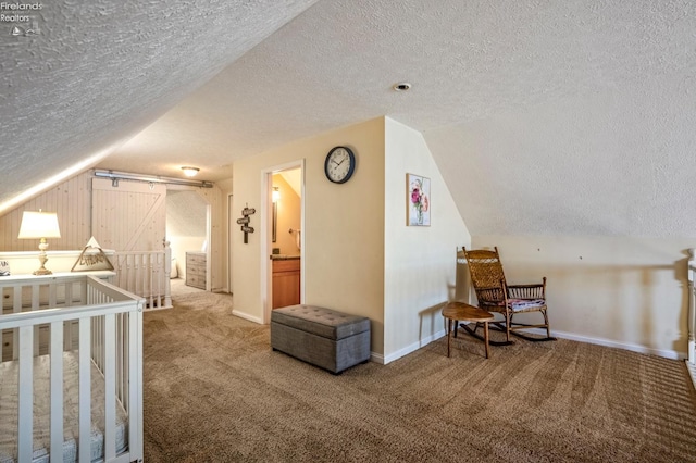 carpeted bedroom featuring a textured ceiling, lofted ceiling, connected bathroom, and a barn door