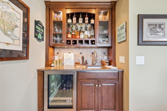 bar with beverage cooler, light stone countertops, sink, and decorative backsplash