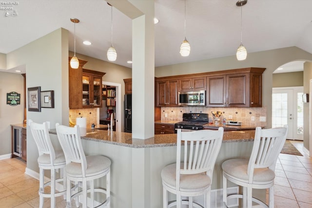 kitchen featuring kitchen peninsula, tasteful backsplash, decorative light fixtures, stone counters, and black gas range oven