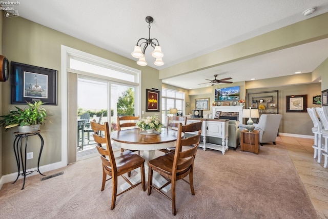 carpeted dining area featuring a stone fireplace and ceiling fan with notable chandelier