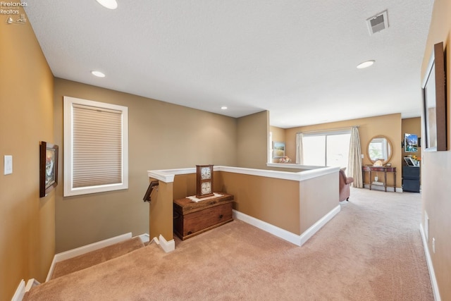 hall with a textured ceiling and light carpet