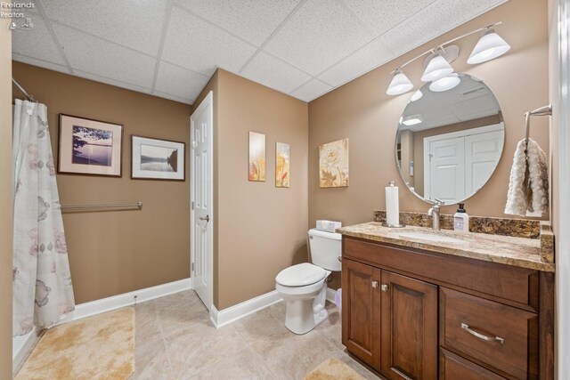 bathroom with a paneled ceiling, walk in shower, tile patterned floors, vanity, and toilet