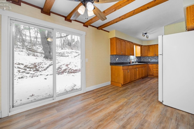 kitchen featuring freestanding refrigerator, light wood-type flooring, a ceiling fan, dark countertops, and brown cabinets