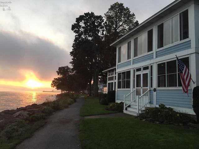 property exterior at dusk featuring a water view, a lawn, and a sunroom