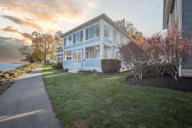 property exterior at dusk featuring a yard, a water view, and a porch