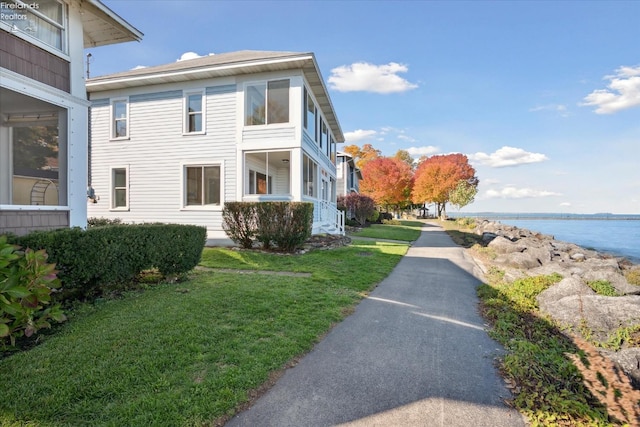 view of property exterior featuring a lawn, a water view, and a balcony