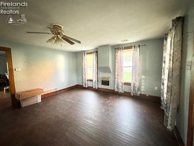 empty room featuring dark wood-type flooring, heating unit, and ceiling fan