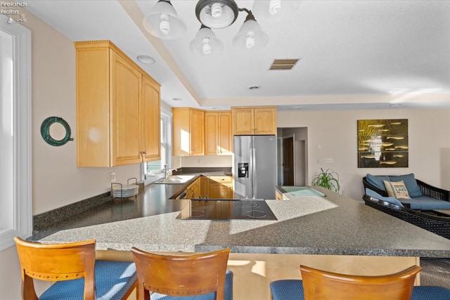 kitchen with stainless steel fridge, kitchen peninsula, light brown cabinets, and a breakfast bar