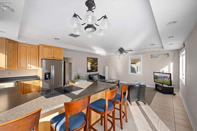 kitchen with ceiling fan, a tray ceiling, light tile patterned flooring, and stainless steel refrigerator with ice dispenser