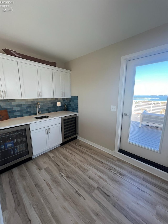 bar with backsplash, sink, beverage cooler, white cabinetry, and light hardwood / wood-style floors