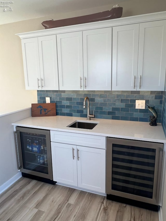 bar with white cabinets, sink, light wood-type flooring, and beverage cooler