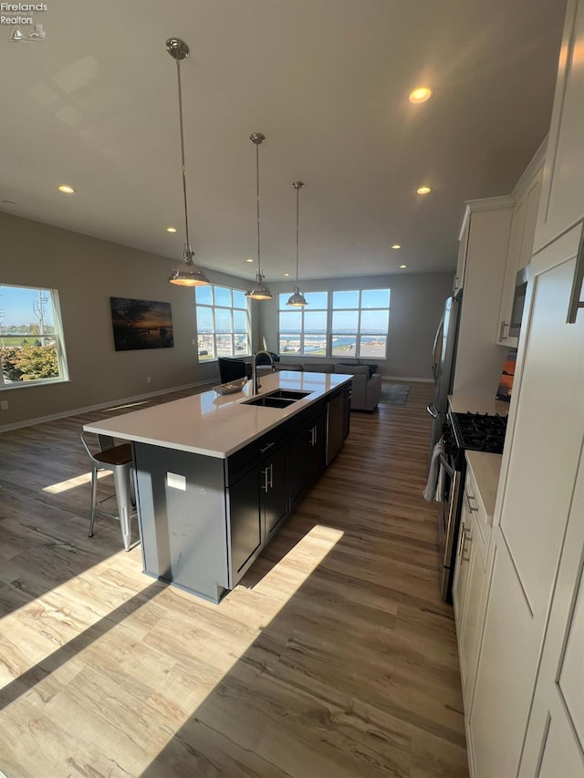 kitchen with a center island with sink, high end range, decorative light fixtures, white cabinets, and light hardwood / wood-style floors