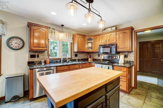 kitchen featuring a kitchen island, sink, butcher block counters, hanging light fixtures, and appliances with stainless steel finishes