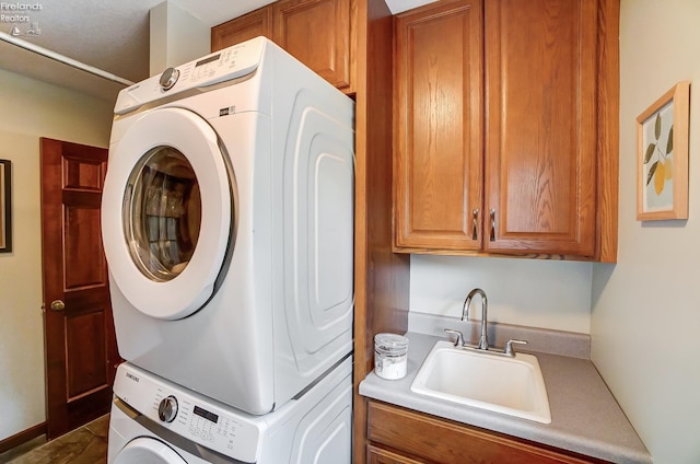 clothes washing area featuring stacked washer and clothes dryer, cabinets, and sink