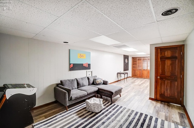 living room with a drop ceiling, wood walls, and hardwood / wood-style floors