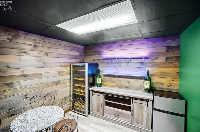 bar featuring a drop ceiling, wine cooler, wood walls, and light hardwood / wood-style floors