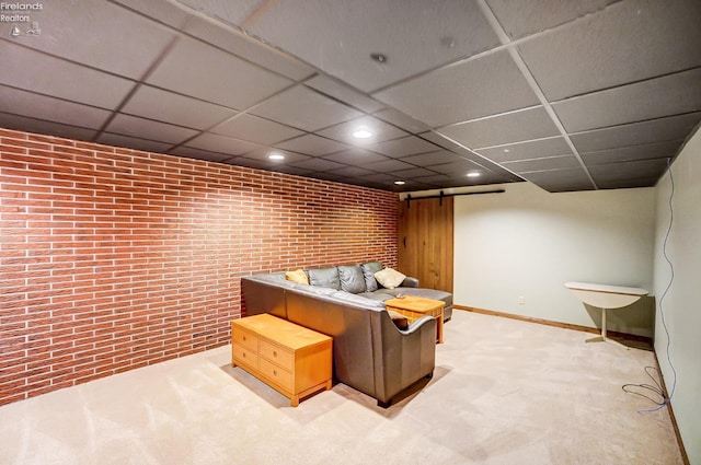 sitting room featuring brick wall, a drop ceiling, a barn door, and carpet