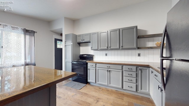 kitchen with gray cabinetry, light wood-type flooring, backsplash, and black appliances