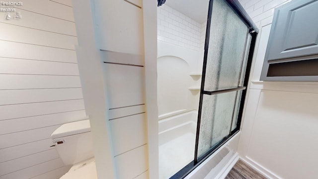 bathroom with bath / shower combo with glass door, wood walls, hardwood / wood-style floors, and toilet