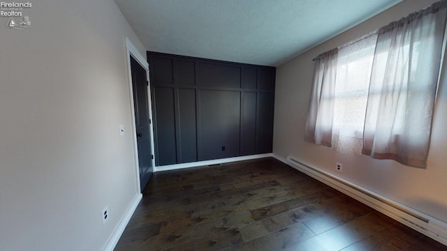 empty room with a textured ceiling, a baseboard heating unit, and dark hardwood / wood-style flooring