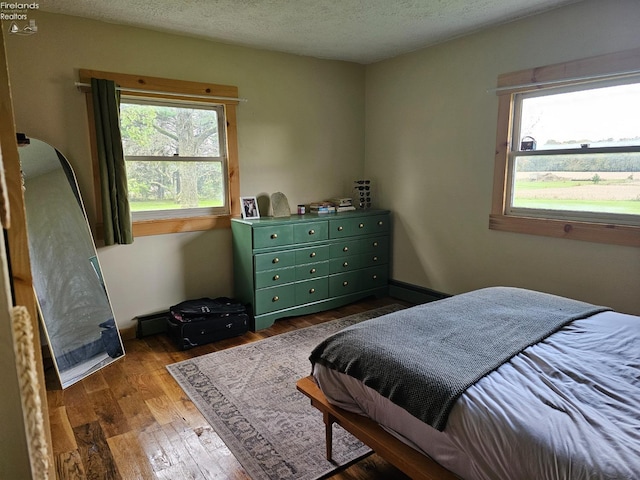 bedroom with a textured ceiling, dark hardwood / wood-style floors, and multiple windows