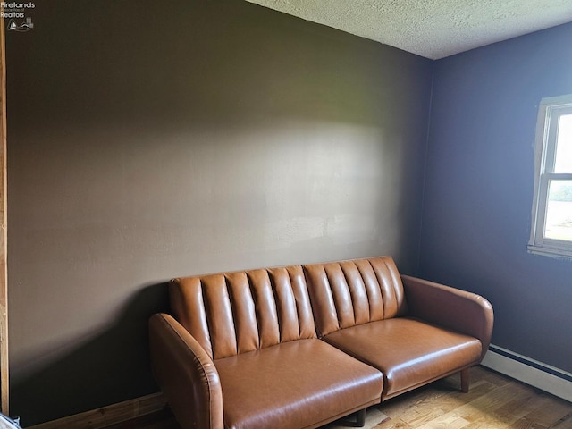 living area with a baseboard heating unit, light wood-type flooring, and a textured ceiling