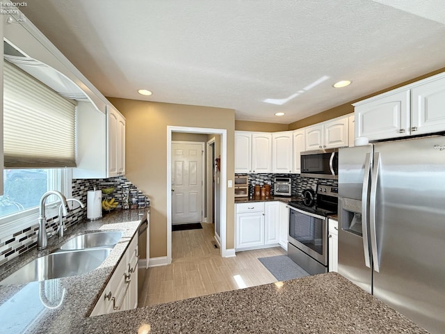 kitchen featuring sink, backsplash, white cabinetry, appliances with stainless steel finishes, and dark stone counters