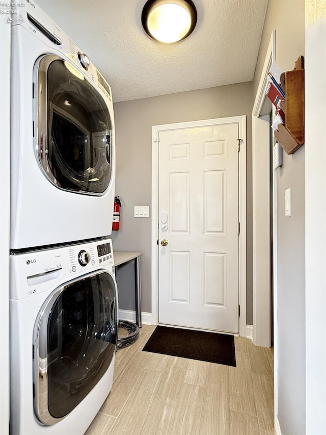 laundry room featuring a textured ceiling, stacked washer / dryer, and light hardwood / wood-style floors