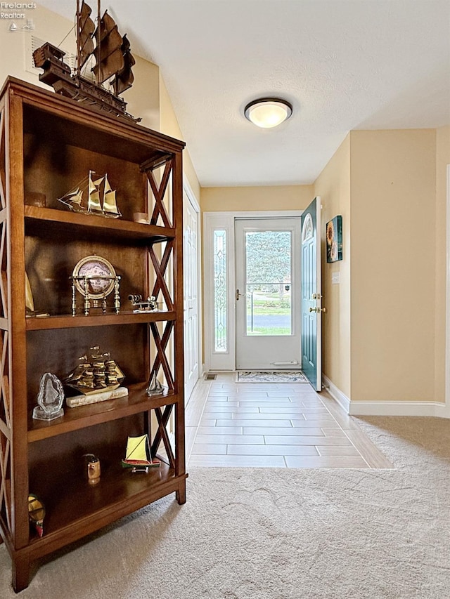 doorway to outside featuring a textured ceiling and light carpet