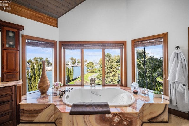 bathroom with a wealth of natural light, a water view, wooden ceiling, and a bathing tub