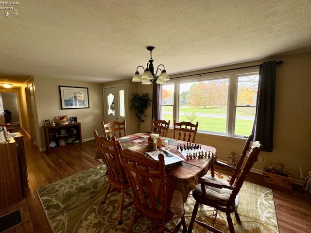 dining room featuring dark wood-type flooring, a textured ceiling, and an inviting chandelier