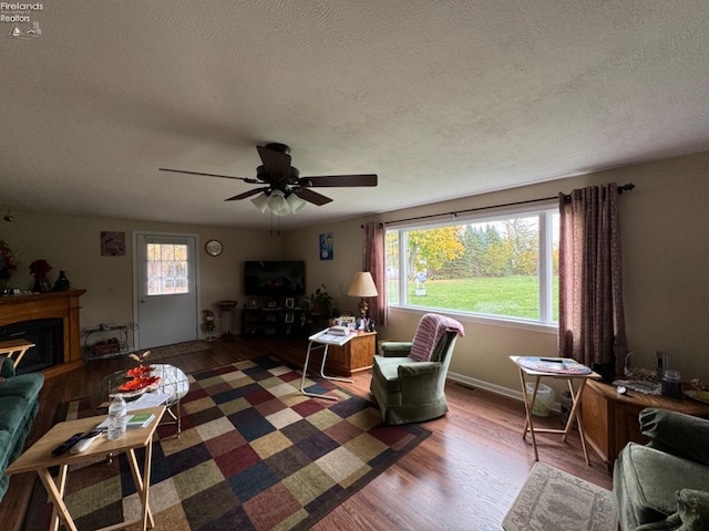 living room featuring dark wood-type flooring, ceiling fan, a healthy amount of sunlight, and a textured ceiling