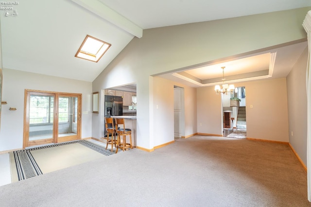 unfurnished living room featuring a notable chandelier, lofted ceiling with skylight, and carpet flooring