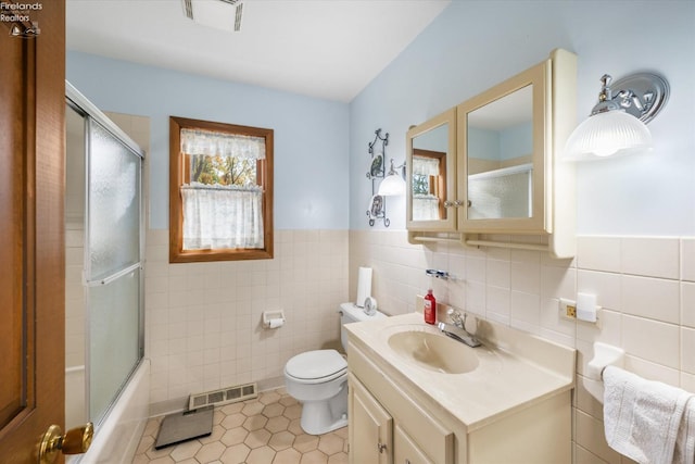 full bathroom with tile patterned floors, toilet, vanity, tile walls, and combined bath / shower with glass door