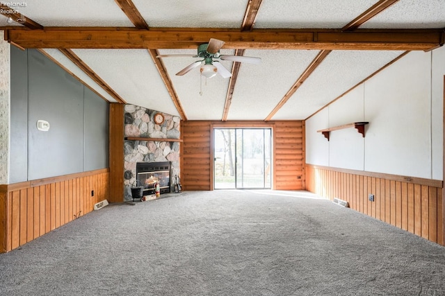 unfurnished living room with ceiling fan, a textured ceiling, carpet flooring, a stone fireplace, and vaulted ceiling with beams