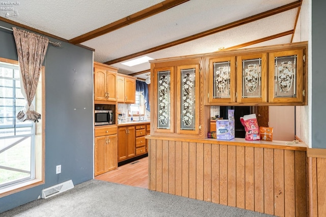 kitchen featuring a textured ceiling, lofted ceiling with beams, wood walls, and a healthy amount of sunlight