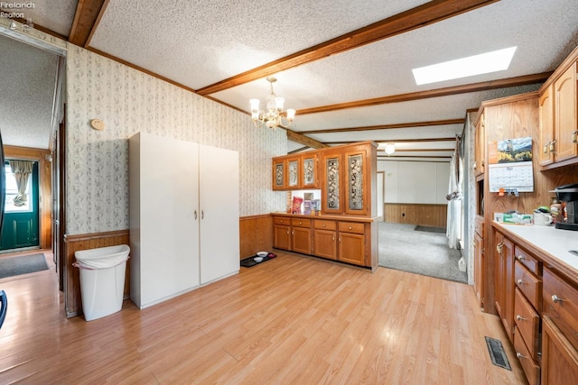 kitchen with a textured ceiling, light wood-type flooring, lofted ceiling with beams, and a notable chandelier