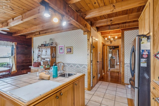 kitchen featuring stainless steel fridge, beam ceiling, light tile patterned floors, tile counters, and sink