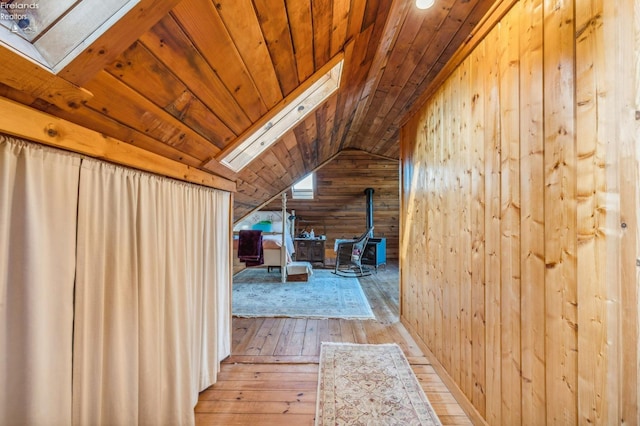 bonus room featuring wooden walls, light hardwood / wood-style flooring, a wood stove, wooden ceiling, and vaulted ceiling with skylight