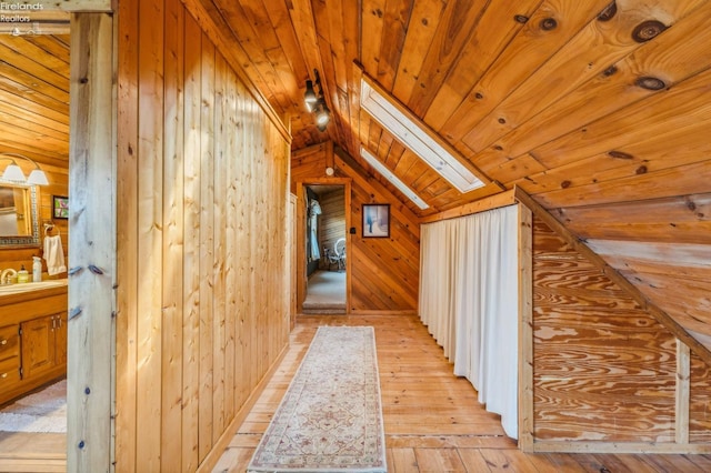 additional living space with sink, wooden ceiling, vaulted ceiling with skylight, wooden walls, and light hardwood / wood-style flooring