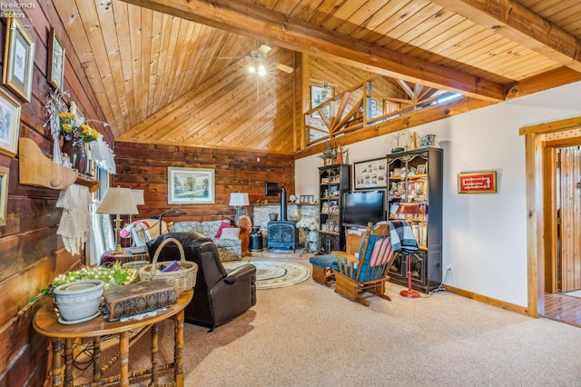 carpeted living room featuring beam ceiling, ceiling fan, wooden ceiling, wood walls, and a wood stove