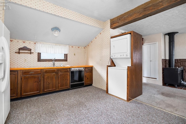 kitchen with black dishwasher, sink, a wood stove, light carpet, and stacked washer and clothes dryer