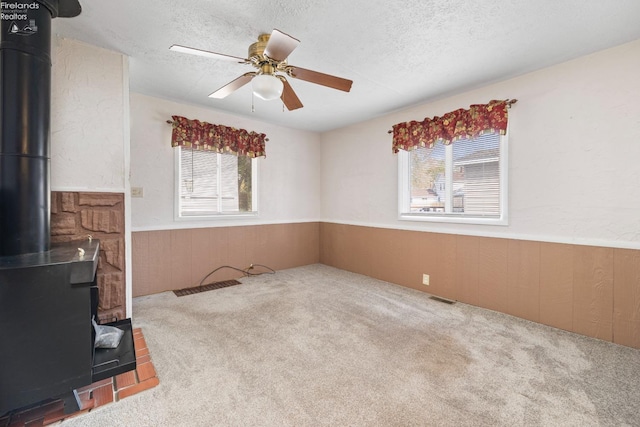 unfurnished room with a wealth of natural light, a textured ceiling, light colored carpet, and a wood stove