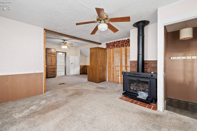 unfurnished living room with ceiling fan, a textured ceiling, carpet floors, and a wood stove