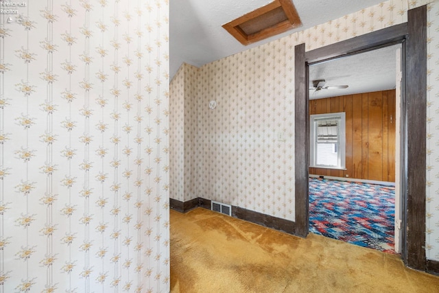 carpeted spare room featuring a textured ceiling, wooden walls, and ceiling fan