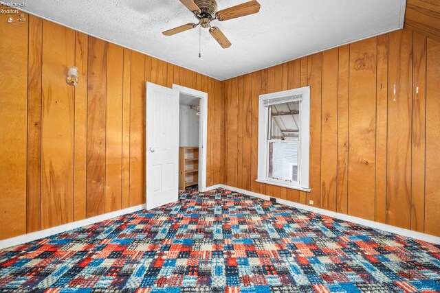 unfurnished bedroom with ceiling fan, a textured ceiling, and wooden walls